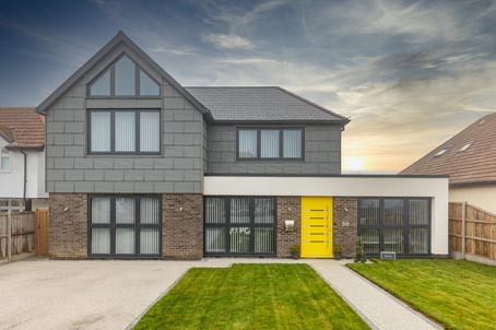 A big house with yellow door and grey windows and cladding