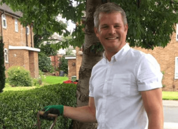 A man standing by a hedge smiling