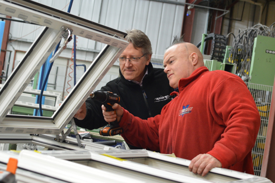 Two men in a factory one with a drill